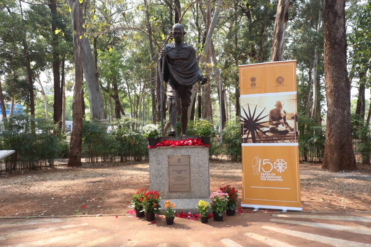 Estátua de Gandhi com banner ao seu lado em homenagem aos seus 150 anos.